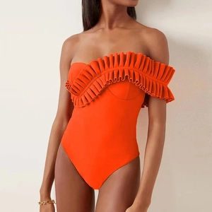 Detail of ruffled flounce on bright orange one-shoulder swimsuit with pleated layers
