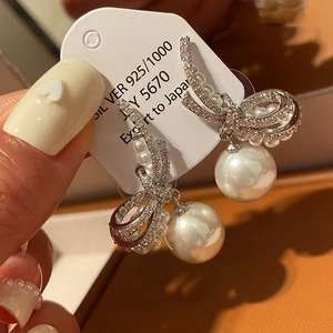 Macro shot of silver bow pearl earrings with zircon inlay on a white jewelry display card