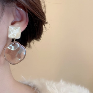 Model wearing geometric resin drop earrings featuring cream textured square and amber charm