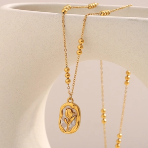 Detail of 18K gold tulip sun pendant on pearl chain necklace against beige ceramic