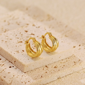 Detailed shot of gold-plated triple hoop earrings on a textured travertine stone base