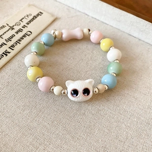 Close-up of macaron color ceramic beaded bracelet with cute cat head bead on textured fabric