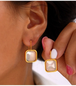Close-up of square gold metal earrings with mother-of-pearl finish on model's hand