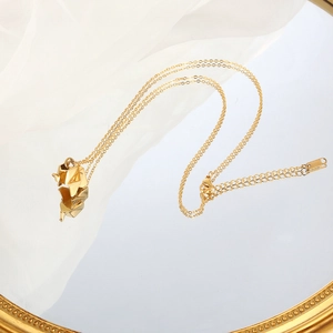 Close-up of gold origami elephant pendant necklace displayed on a mirrored surface