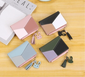 Detail of color-block zip wallets with fringe tassels and bunny charms on wood surface