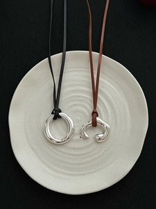 Detail view of mirror-polished silver pendants on leather cords over a ceramic plate