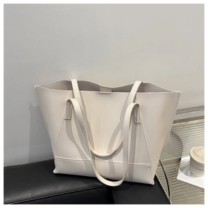 Dettaglio di una borsa tote bianco crema accanto a una tazza di caffè e una rivista trendy