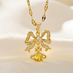 Detail of gold bow necklace with yellow orb pendant on soft silk texture background
