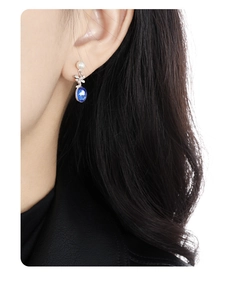 Detailed view of elegant earrings with blue oval gemstone, pearl and floral accents