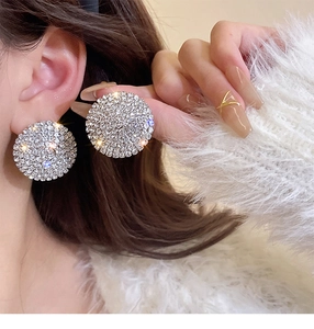 Close-up of oversized sparkling silver round stud earrings with pavé crystals on model