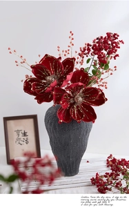 Close-up of red velvet artificial flowers with gold glitter in a textured stone vase