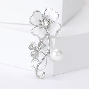 Detailed close-up of clover brooch with shell inlay and pearl on white geometric stands