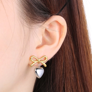 Close-up of golden bow and silver heart pendant earring worn by a model
