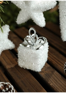 Close-up of white glitter gift box ornament with silver bow on rustic pine background