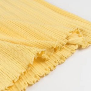 Détail du tissu en maille côtelée jaune montrant la texture et l'ourlet à volants