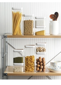 Airtight pantry containers for pasta and grains on a two-tier wooden kitchen shelf