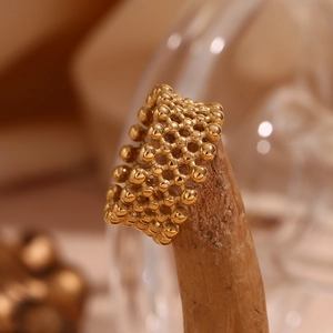 Macro detail of a 18K gold-plated beaded mesh ring displayed on a wooden stand