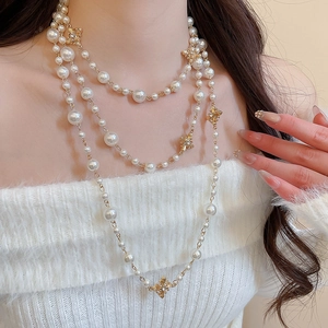 Detailed view of multilayer French pearl necklace with golden floral accents on model