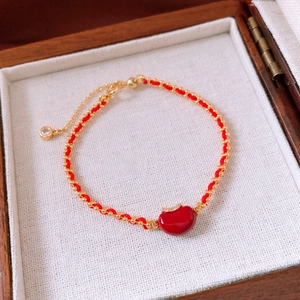 Detail eines roten gewebten Armbands mit Goldperlen, Zirkonia-Apfel und verstellbarer Kette