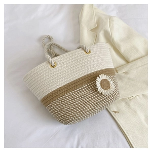 Detailed shot of a beige woven tote bag with daisy ornament and rope handles on white linen