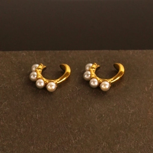 Golden C-shaped earrings with five white pearls set on a textured dark background
