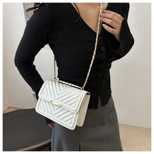 Detail of white V-quilted flap bag with gold chain strap worn by a model in a grey skirt