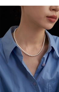 Close-up of a vintage single-strand pearl necklace on a model with a blue shirt