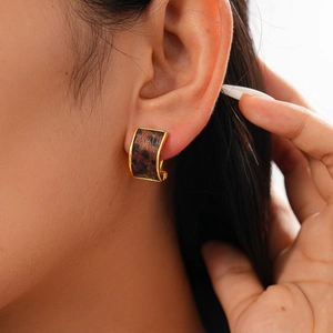 Detailed view of leopard print earring with gold trim worn by a fashion model