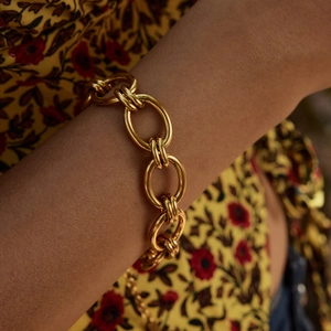 Détail d'un bracelet gourmette doré en acier inoxydable porté sur fond floral chaud