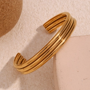 Macro detail of triple-layer 18K gold plated stainless steel open bangle on stone surface