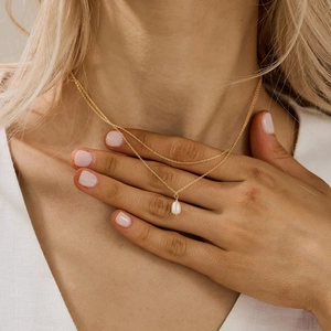 Detail of elegant double-layered gold necklace with a white drop pearl pendant on a model