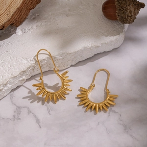 Detail of sunburst gold earrings on natural stone with a warm aesthetic lighting