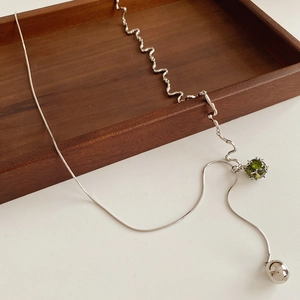 Detail einer silbernen Schlangenkette mit grünem Edelstein und gewelltem Metallglied