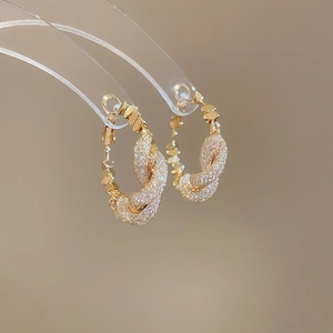 Close-up of twisted golden hoop earrings with pavé zircons on an acrylic stand