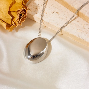 Minimalist silver oval pendant necklace displayed on silk fabric with beige stone