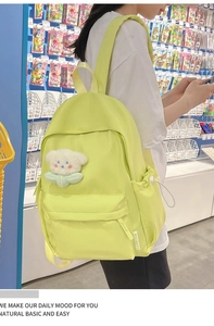 Detail view of a neon yellow nylon backpack featuring a cute white plush bear keychain