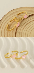 Detail of pink enamel heart and dolphin open rings in gold finish on natural wood background