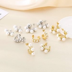 Macro detail of C-shaped stainless steel earrings with elegant white pearls on beige fabric