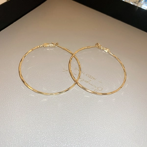 Detail of large golden hoop earrings with hammered texture and pin closure design