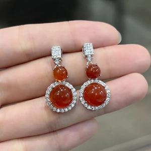 Close-up of hand holding silver earrings set with round red-orange chalcedony and zircons