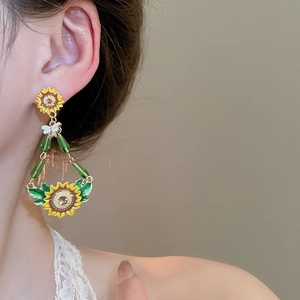 Close-up of sunflower and bee earrings with green enamel leaves on a female model