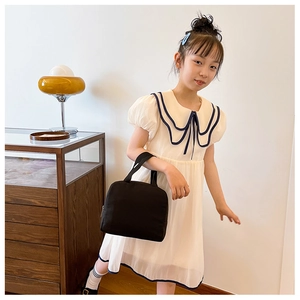 Detail of a minimalist black thermal lunch bag held by a girl in a white dress