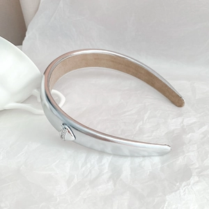 Close-up of wide silver metallic headband with rhinestone heart detail and beige lining