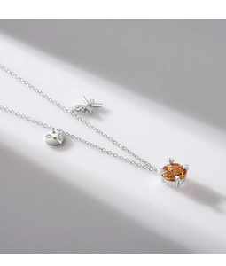 Detailed shot of silver necklace with orange gemstone, butterfly and disc charms