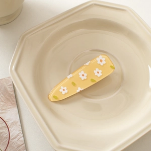 Macro detail of yellow acrylic hair clip with white daisy floral pattern on a plate