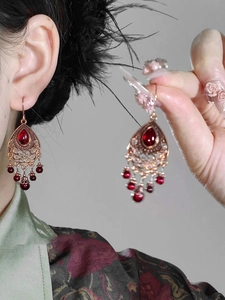Detailed view of vintage bronze earrings with red beads and intricate filigree patterns