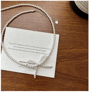 Macro shot of silver bow pearl necklace on dark wood with romance card and candle