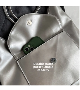 Detail view of silver metallic tote bag featuring a front pocket for smartphone storage