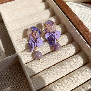 Macro shot of purple floral resin drop earrings on beige velvet jewelry box