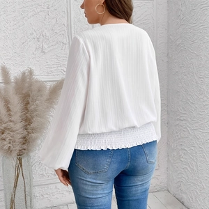 Detailed view of the white long-sleeve blouse featuring smocked waist and textured fabric